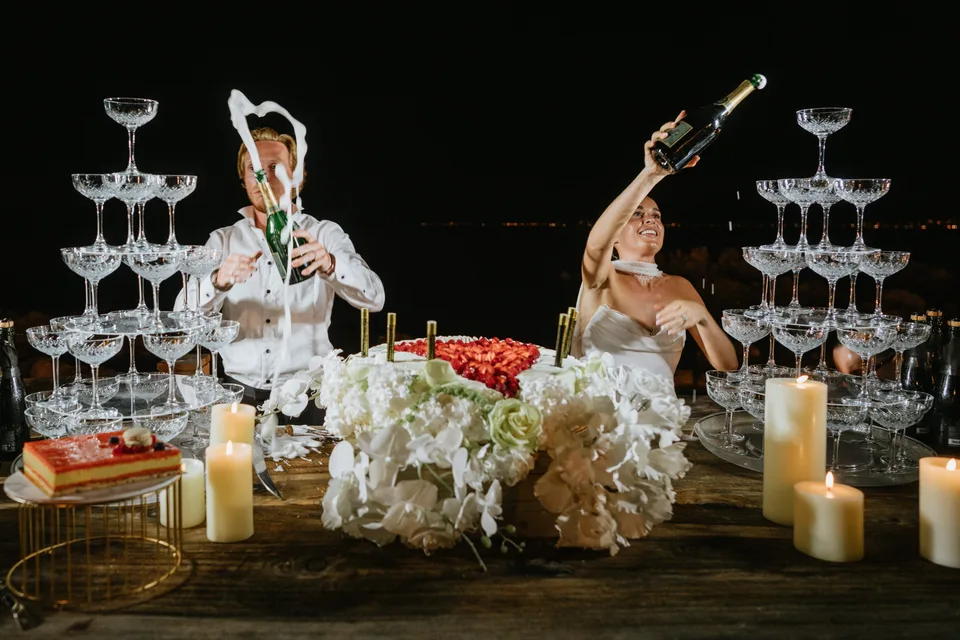 Newlyweds raising their arms beside champagne glasses