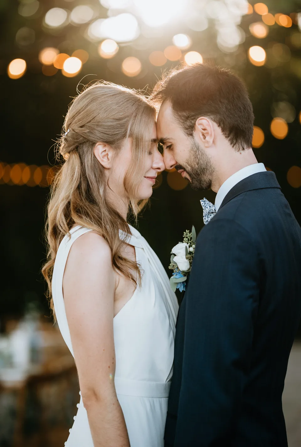 Newlyweds forehead to forehead beneath string lights
