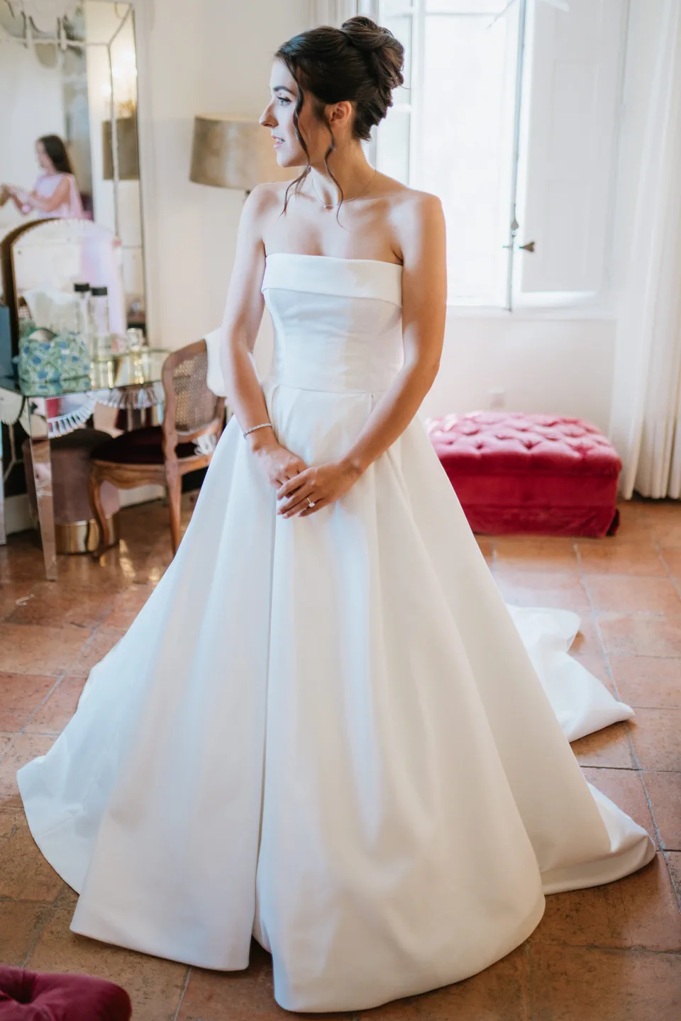 The bride holding her dress beside a window
