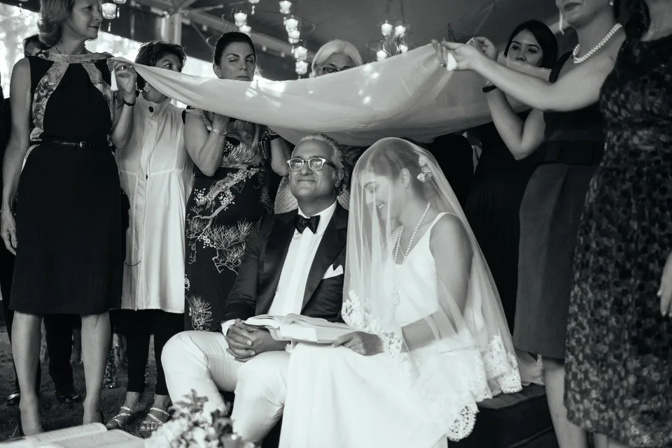 Newlyweds beneath a veil held by loved ones, in black and white