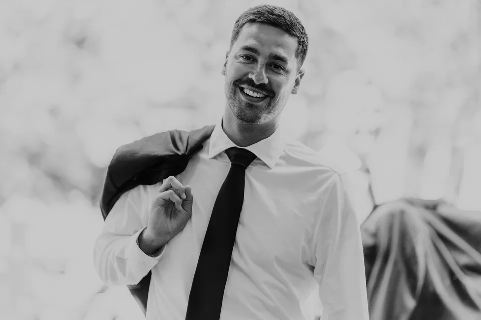 The groom smiling while adjusting his outfit, in black and white