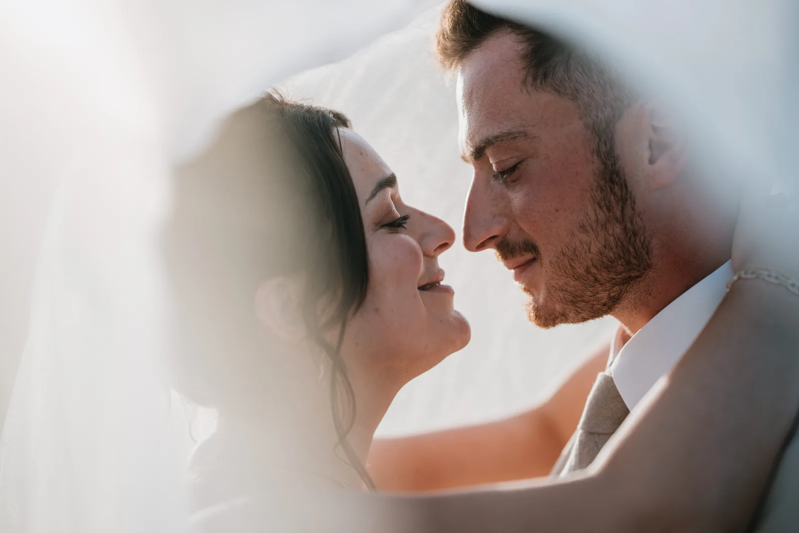 Newlyweds leaning towards each other beneath the veil