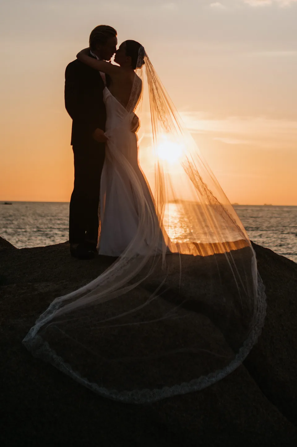 Newlyweds and veil silhouetted against the sunset