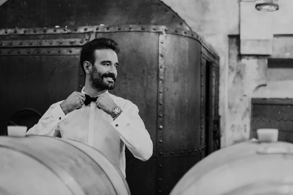 The groom adjusting his bow tie in the mirror, in black and white