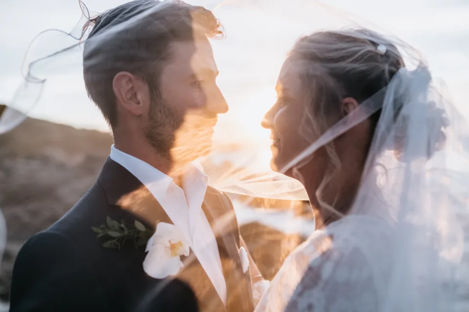 Newlyweds’ faces beneath the veil in evening light