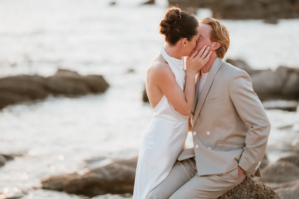 Newlyweds kissing on rocks beside the water